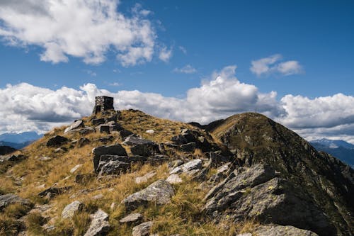 High rocky peak of mountain with rough uneven stones under cloudy blue sky in sunny day