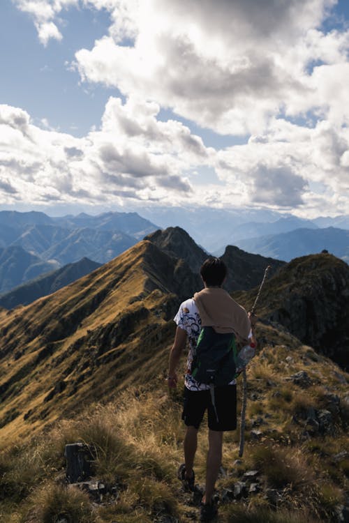 Free Back view full body of faceless man standing on top of ridge with growing grass in mountainous terrain Stock Photo
