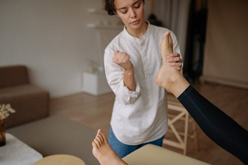 Free Woman in White Long Sleeve Shirt Massaging the Feet of Another Person Stock Photo