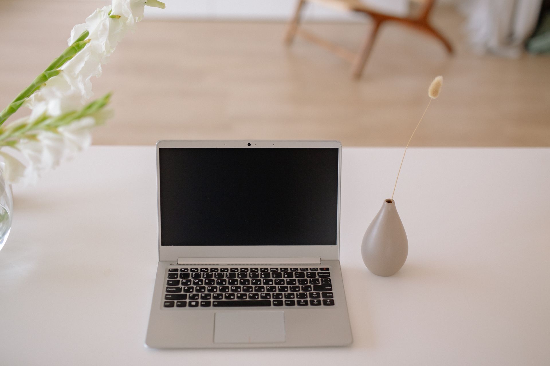 Stylish home office desk featuring a laptop, vase, and decorative plants in a minimalist setting.