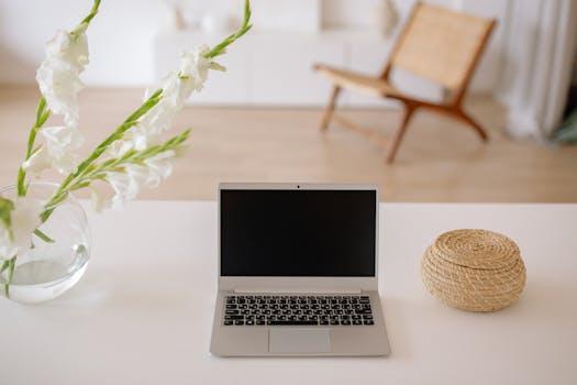 A serene home office space featuring a laptop, white flowers, and wicker basket on a desk.