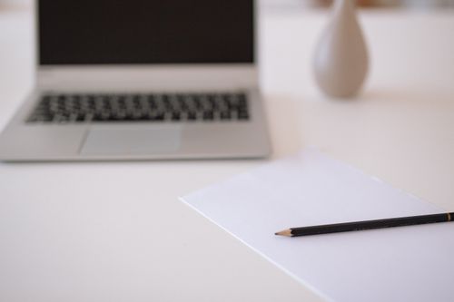 Free A minimalistic workspace featuring a laptop, blank paper, and pencil on a white table. Stock Photo
