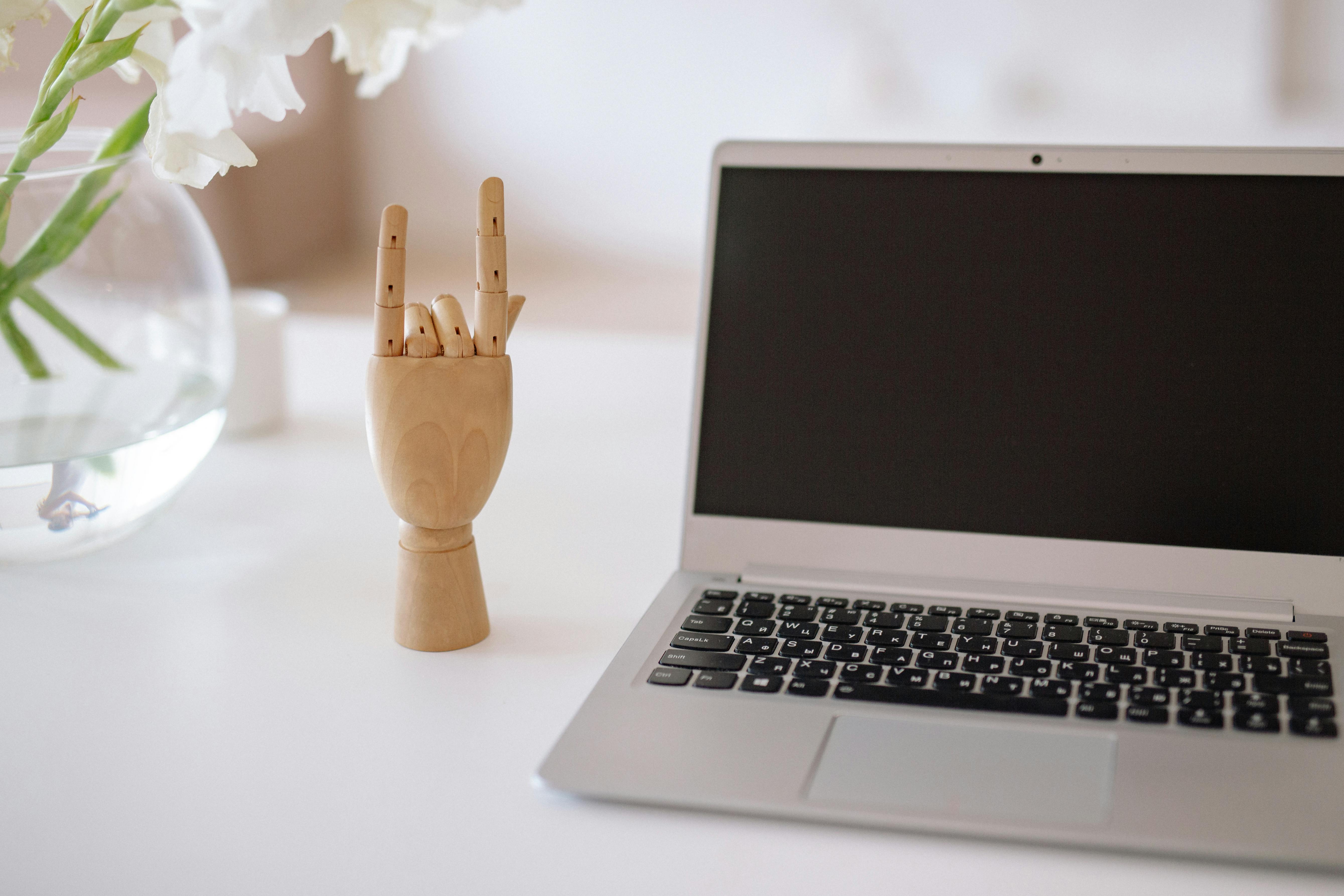 A minimalist desk setup featuring a laptop and a wooden hand sculpture, perfect for creative workspaces.