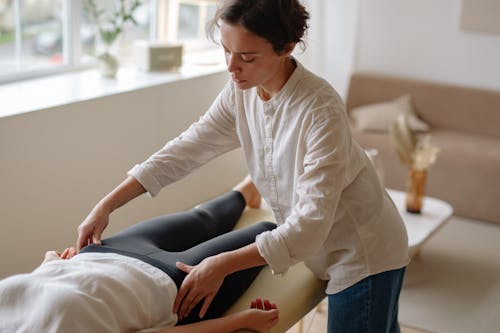 Free Woman in White Long Sleeve Shirt Massaging a Person's Hips Stock Photo