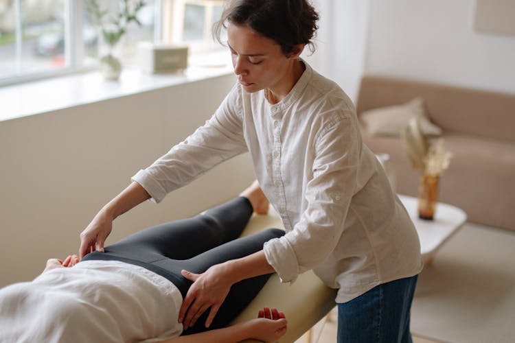 Woman In White Long Sleeve Shirt Massaging A Person's Hips