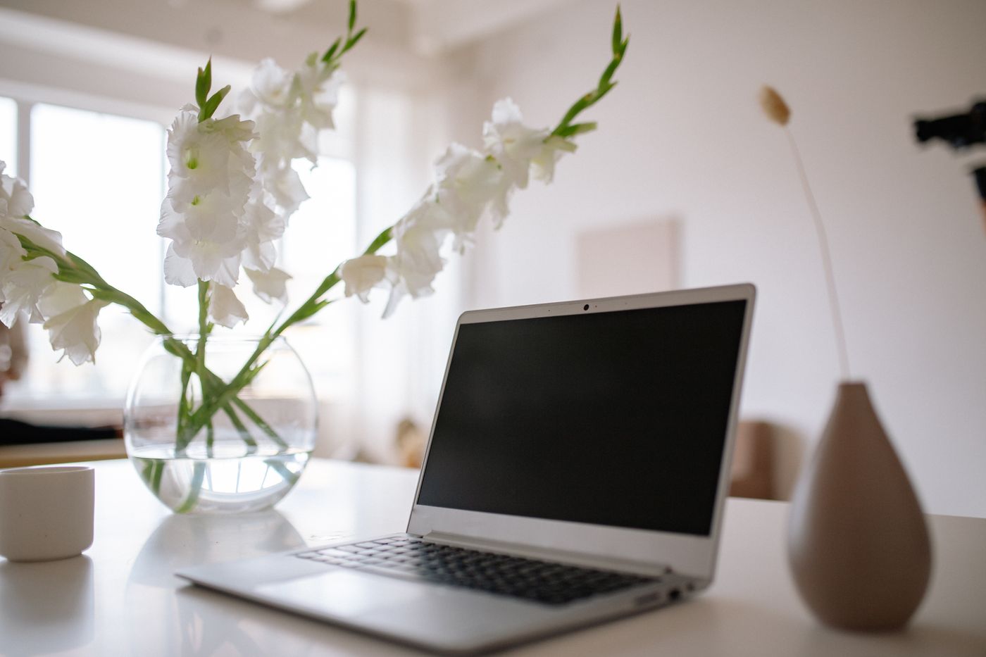 A quiet, sunlit desk — laptop, white blooms, ready for a session