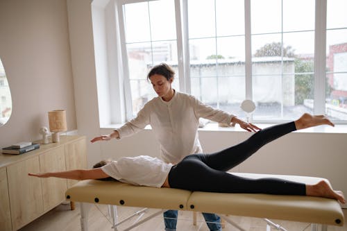 Free A Woman in White Top and Black Leggings Lying on a Massage Table Stock Photo