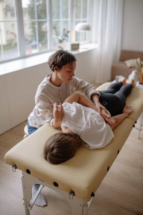 Free A Therapist Holding a Woman's Hand Lying on a Massage Table Stock Photo