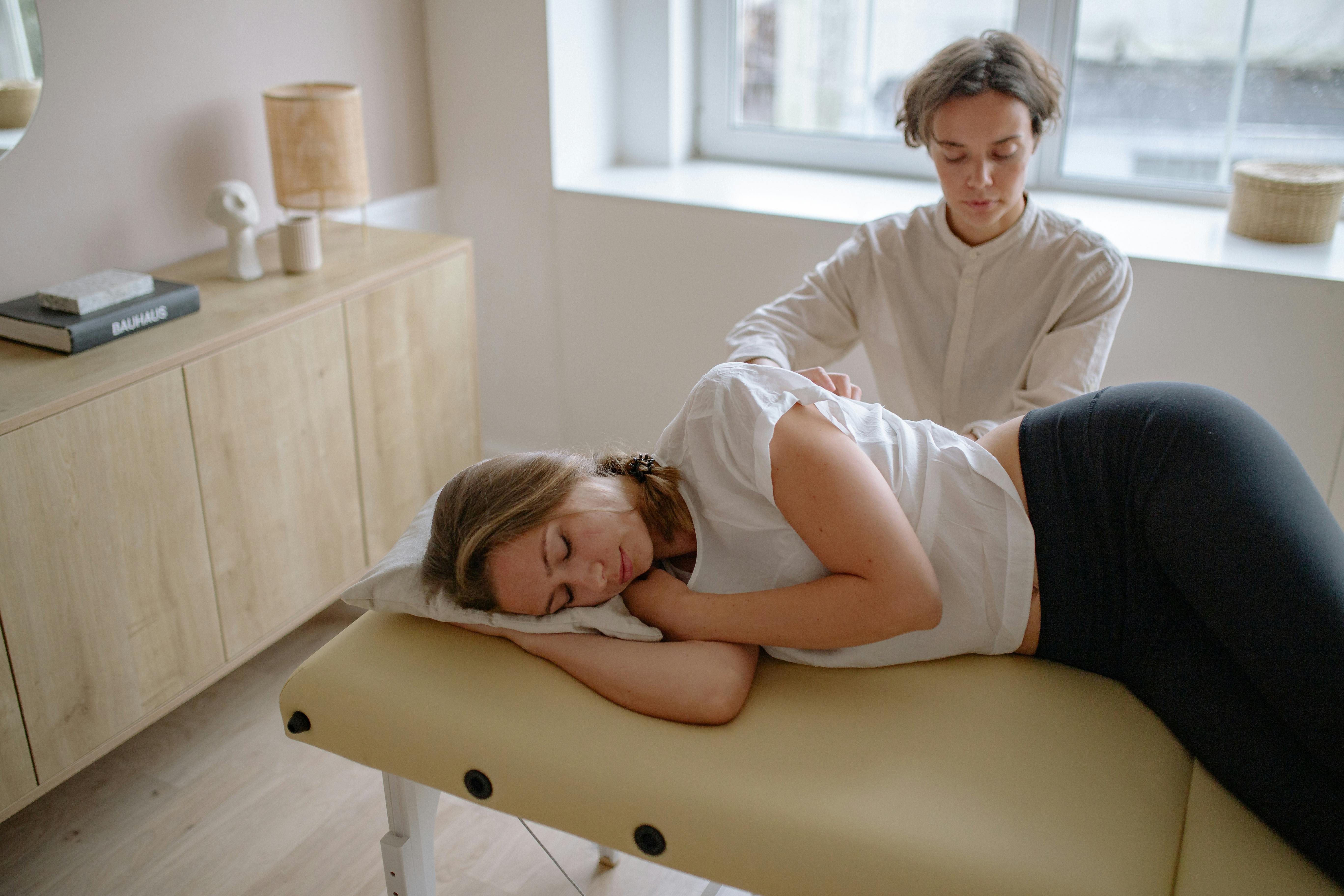 a woman in long sleeves massaging a woman lying on bed