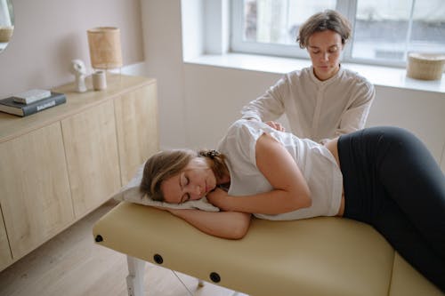 Free A Woman in Long Sleeves Massaging a Woman Lying on Bed Stock Photo