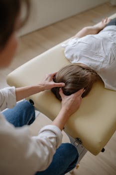 A chiropractor performing a therapeutic head massage on a woman lying on a massage table.