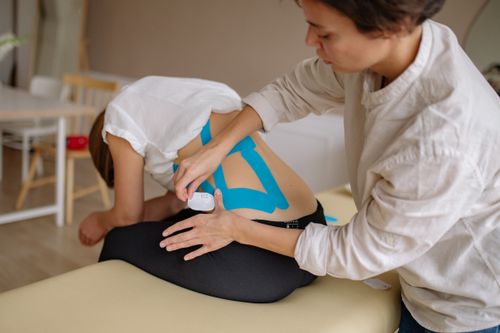 Free A therapist applies blue kinesiology tape to a patient's back in a clinical setting. Stock Photo