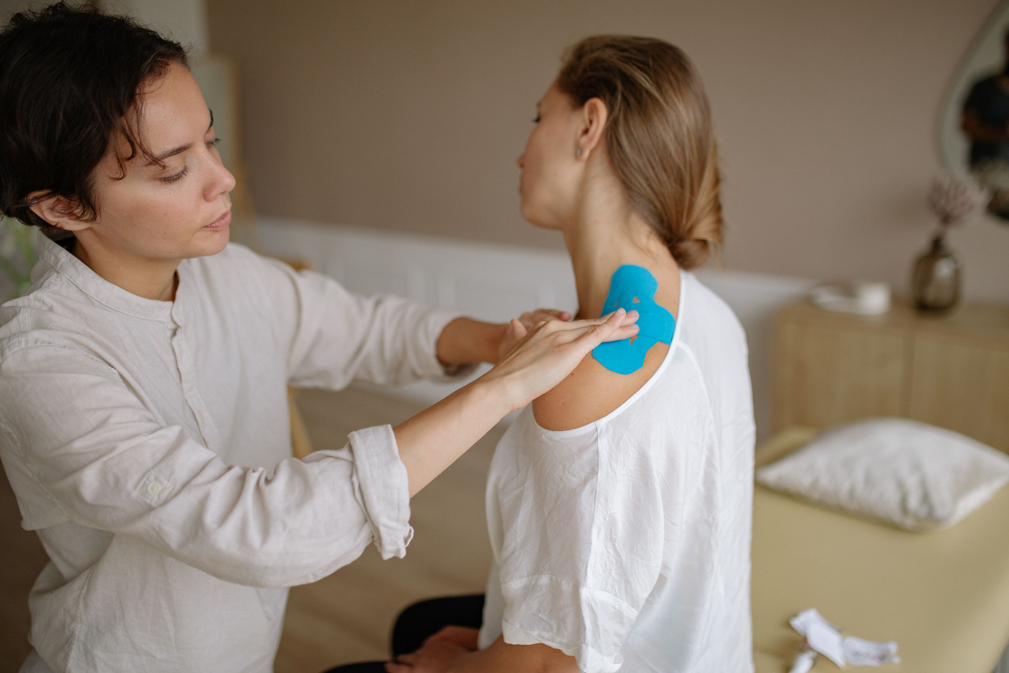 Elena taping a patient's shoulder in the treatment room