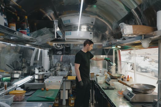 A man preparing food inside a stainless steel interior food truck kitchen.