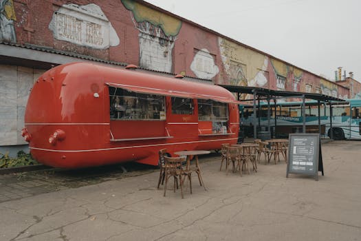 Red food truck with tables in a colorful urban environment with graffiti walls.