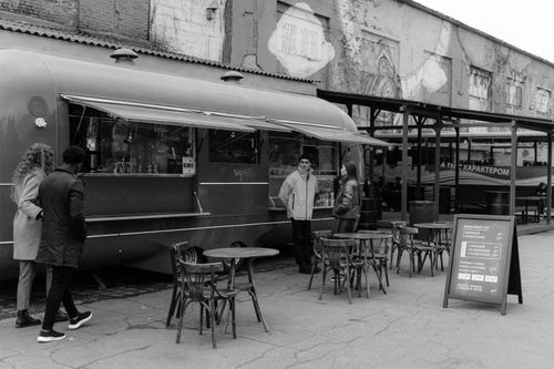 Free Black and white urban scene featuring a food truck with people and outdoor seating. Stock Photo