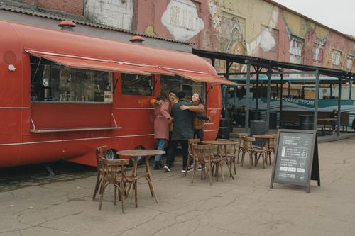 Free A group of friends hug in front of a red food truck with street art surroundings. Stock Photo