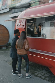Two people ordering food at a vibrant red food truck on a street during the day.