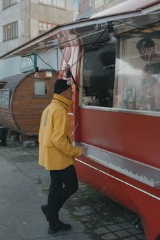 一名身穿黄色夹克的男子在街边向一辆红色餐车点餐