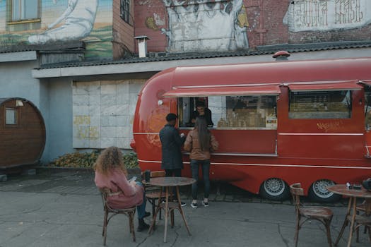 A vibrant urban scene with a red food truck serving people on the street, offering an authentic street food experience.