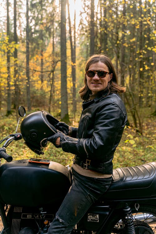 Free A Man Sitting on His Parked Motorcycle Holding a Helmet Stock Photo