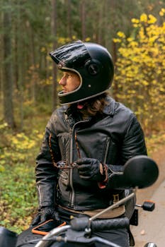Biker with helmet and leather jacket sitting on a motorcycle in an autumn forest.