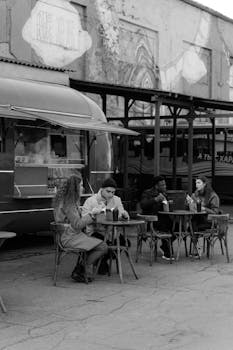 Grayscale image of friends enjoying food by a food truck on a street.