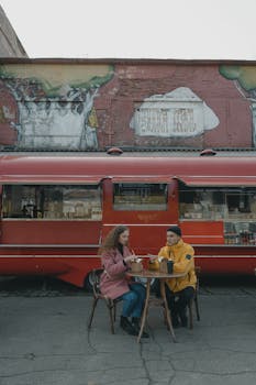 A couple dining near a bright red food truck on a cool day, sharing a meal.
