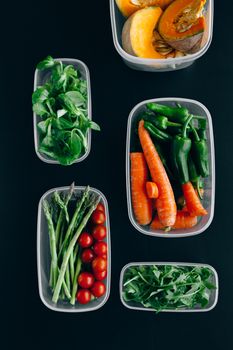 Assorted fresh vegetables in plastic containers on a dark surface, perfect for healthy eating.