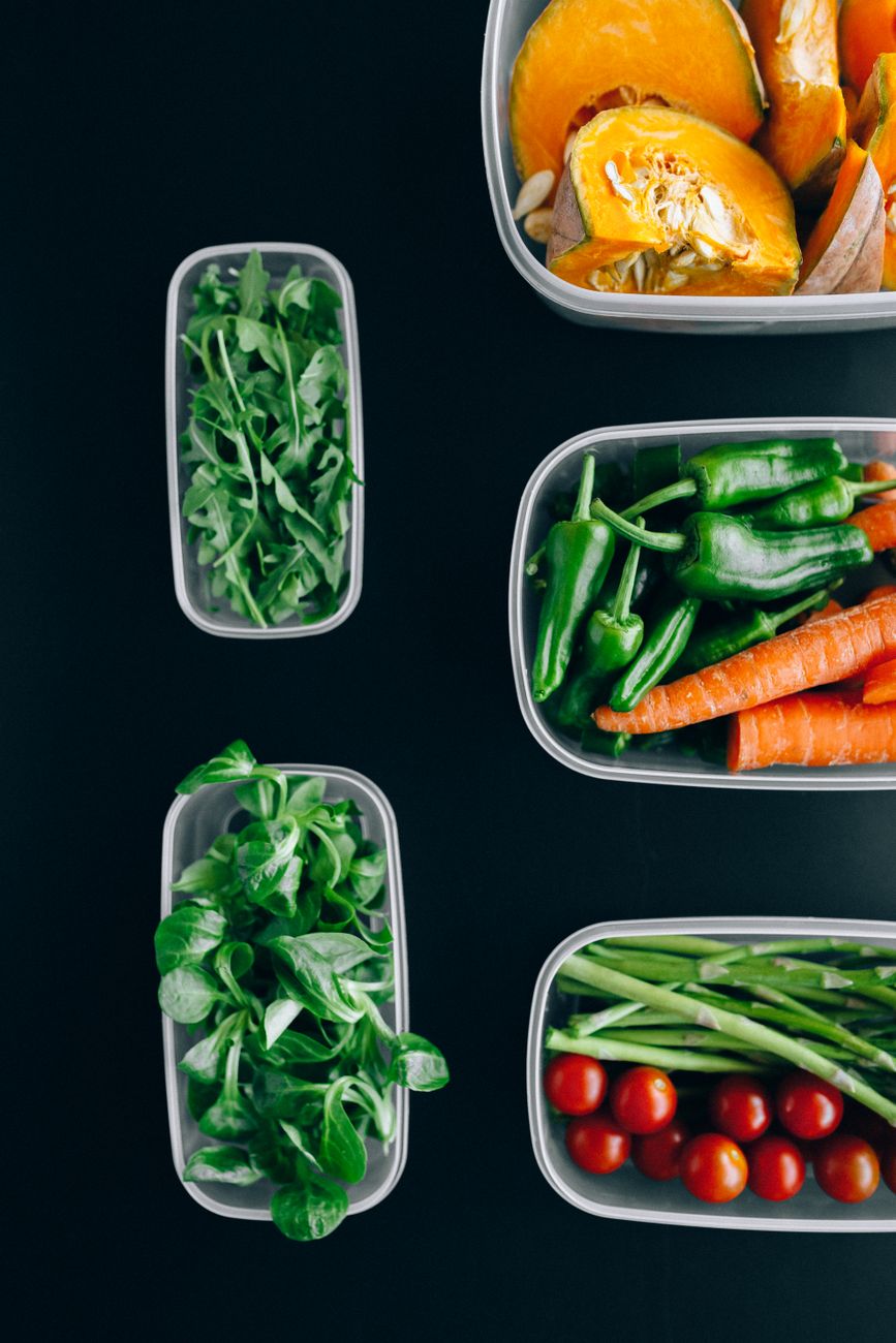 Vibrant assortment of fresh vegetables in plastic containers on a black background, showcasing healthy eating.