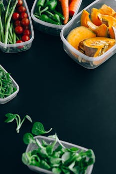 Overhead view of assorted fresh vegetables in plastic containers against a black backdrop.