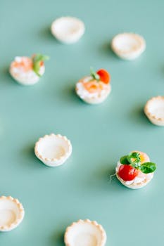 Delicious mini tart shells topped with cherry tomatoes and herbs on a green background.