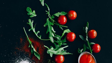 A vibrant flatlay of Italian ingredients featuring pasta, cherry tomatoes, and arugula on a dark background.