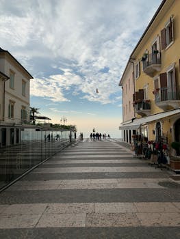Charming street scene in Lazise, Italy with rustic balconies and a view of Lake Garda under a cloudy sky.
