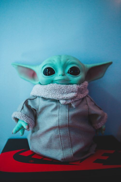 Free Small collectible green figure of character from famous movie placed near white wall in room with neon illumination Stock Photo