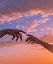 Crop anonymous people pulling hands to each other against bright sunset sky with clouds