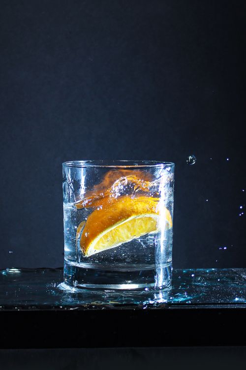 Free A glass of water with a lemon slice splashing, captured against a dark background. Stock Photo