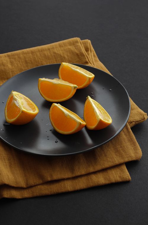 Free Top view of fresh orange slices on a stylish black plate with a brown cloth backdrop. Stock Photo