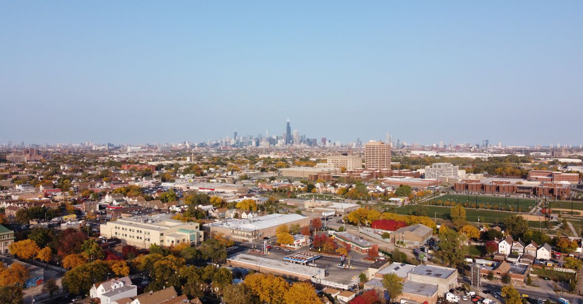 Drone shot capturing the sprawling Chicago skyline with colorful suburban landscape in the foreground.