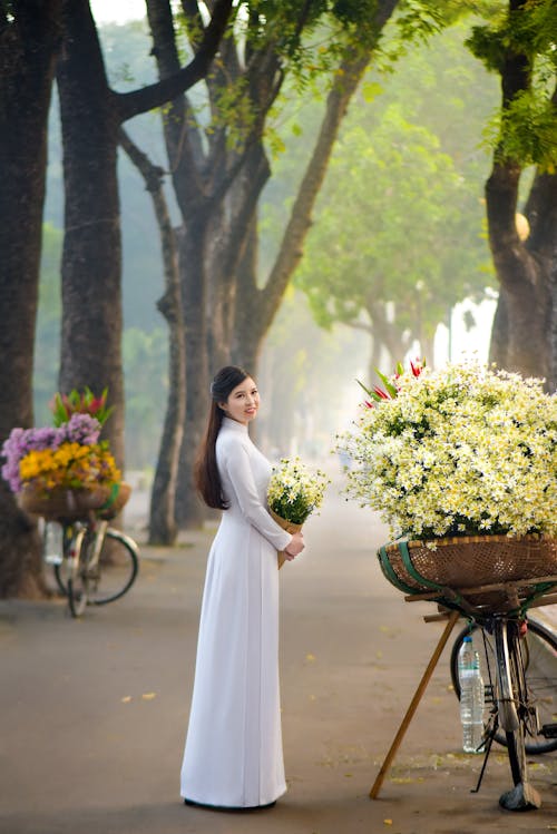 A Woman Wearing White Ao Dai while Holding a Bouquet of Flowers