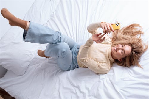 Happy woman lying on bed and using smartphone