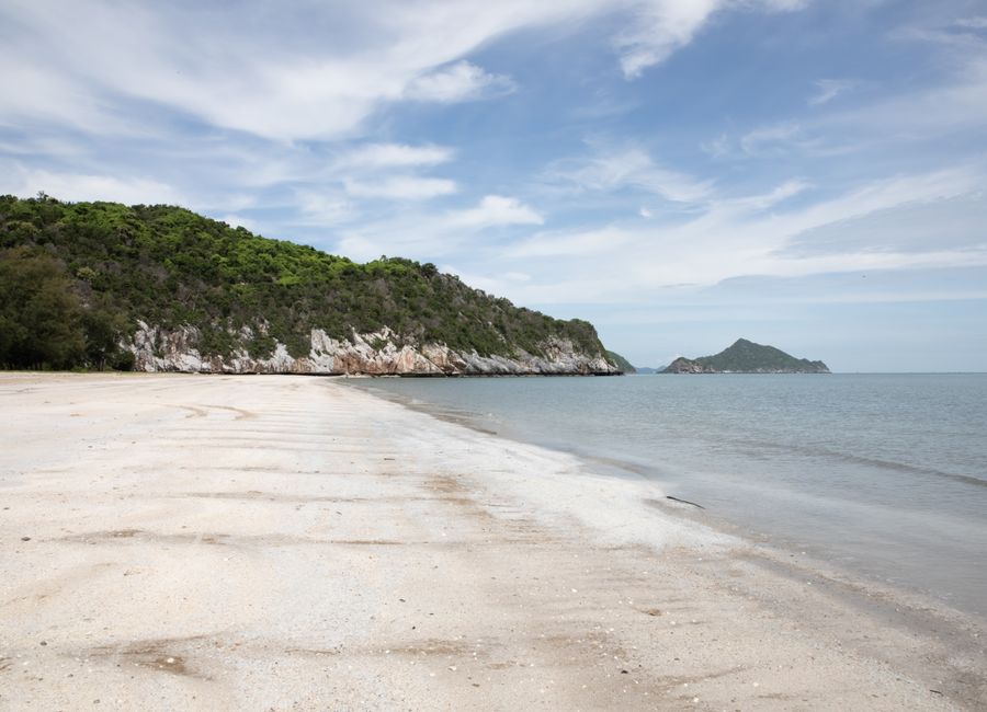 Explore the pristine white sand beach along the lush, rocky shoreline of Thailand's coastal beauty.