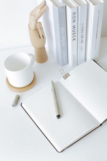 An open notebook with a pen resting near a mug and books