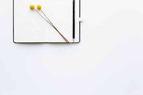 Free Top view composition of pencil and creative bookmarks placed on opened diary with blank sheets on white desk Stock Photo