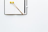Top view composition of pencil and creative bookmarks placed on opened diary with blank sheets on white desk