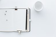 Top view composition of opened diary with blank pages placed on white desk with pencil and paintbrush pins