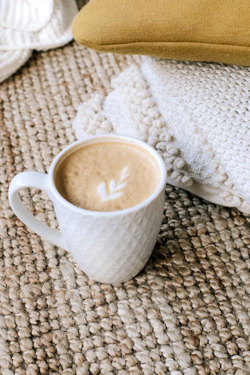 Free From above white ceramic mug of fresh hot cappuccino placed on soft knitted plaid near pillows Stock Photo