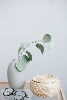 玻璃桌上，靠近眼镜的地方，放着一个浅蓝色花瓶，里面插着柳条篮和绿色植物的枝条