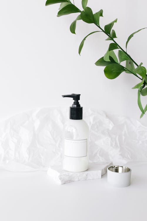 Arrangement of plastic jar with body cream placed on white table near green lush plant