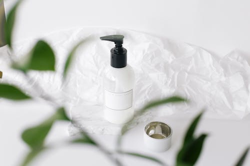 High angle through plant leaves view of plastic bottle with moisturizing lotion placed on white table